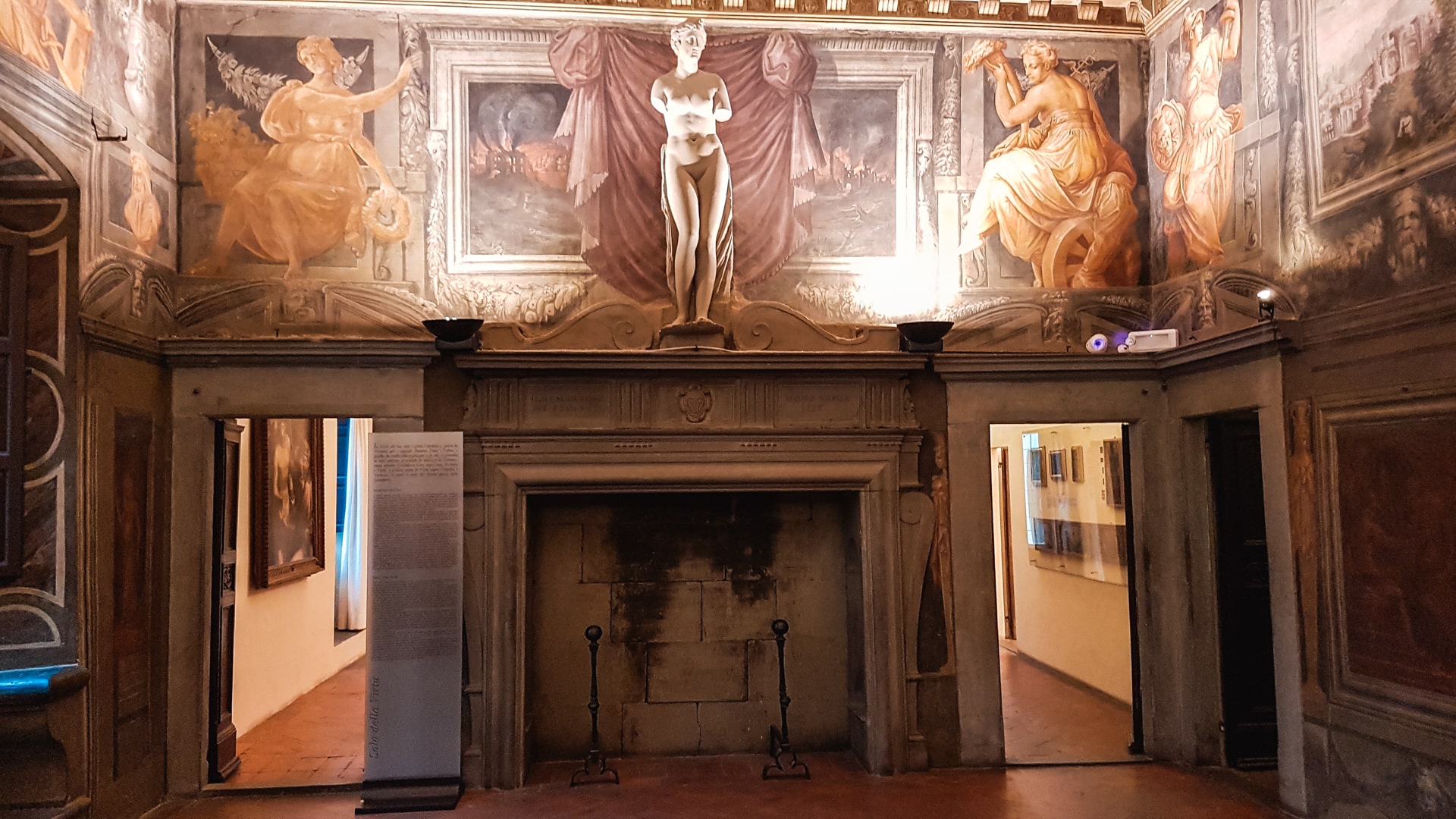 Una bellissima sala della casa vasari di arezzo. In primo piano un camino incorniciato e sopra affreschi decorativi e una statua in marmo.