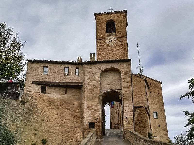 L'ingresso al borgo di Montegridolfo in provincia di Rimini. L'alta porta medievale fa spazio ad una straducola che porta dentro il centro storico. Sopra si staglia sul cielo l'alta torre dell'orologio.