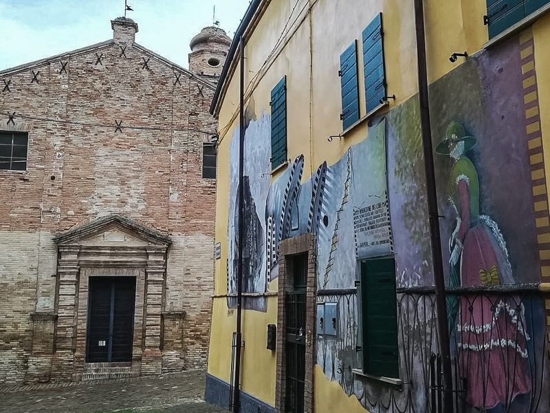 Saludecio è forse una delle destinazioni più curiose nella provincia di rimini. Si nota nella foto dei murales disegnati su un edificio giallo e accanto un antica chiesetta medievale costruita in pietra.