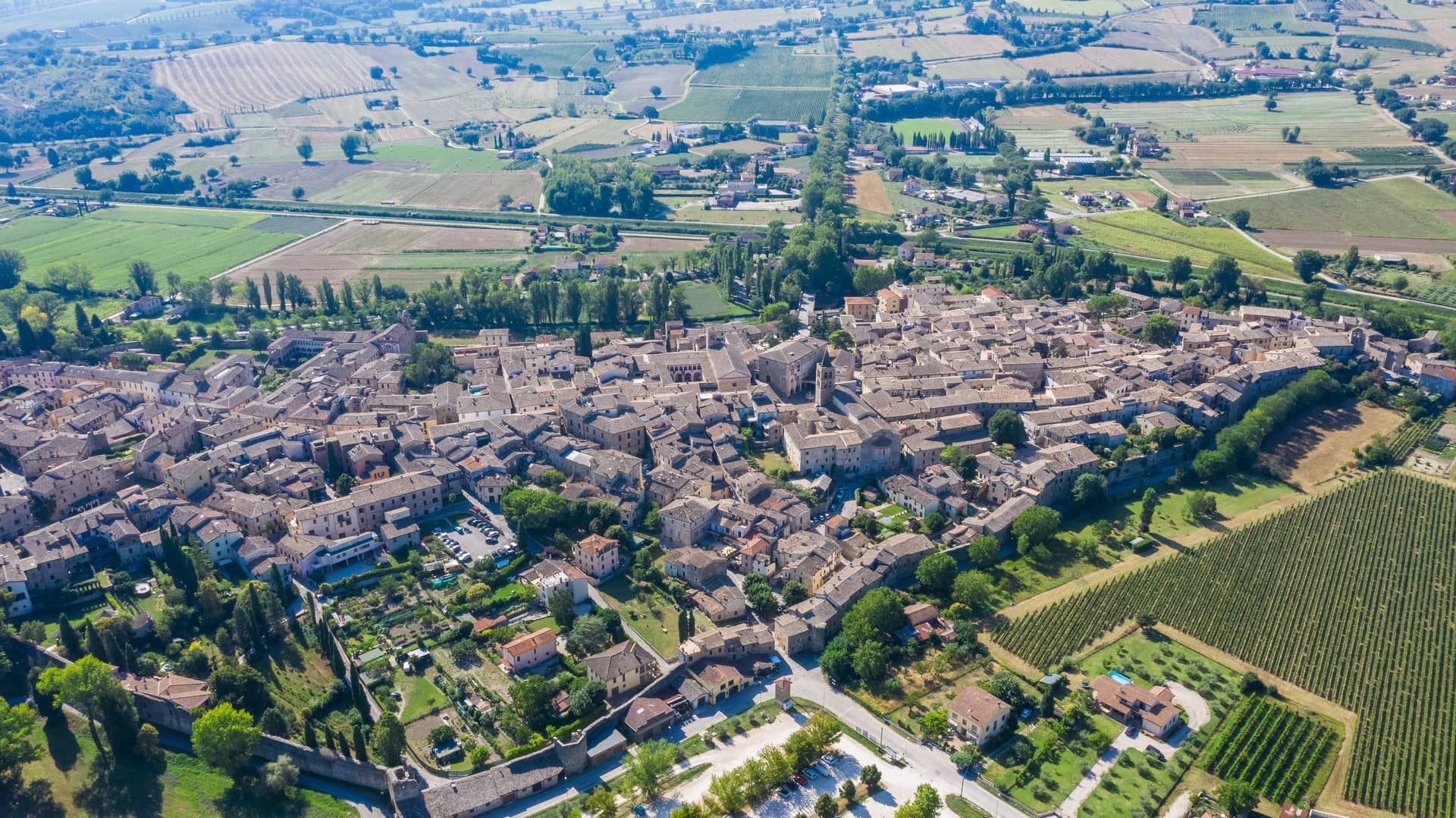 La vista dall'alto di Bevagna, il borgo medievale umbro. Si può notare la sua forma a fortezza con le tante case medievali tutte incorporate al centro. Intorno il verde delle coltivazioni e dei colli.