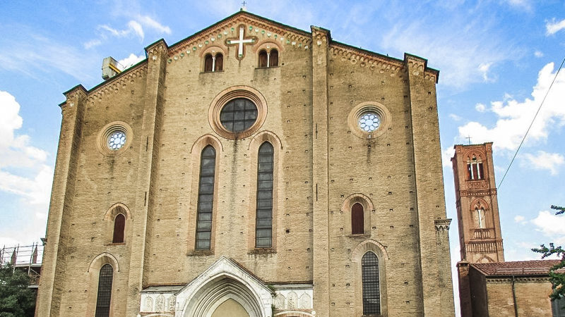 L'imponente e altissima facciata della basilica di san francesco a bologna, tutta costruita in mattoni. In cima un rosone e sopra una croce. Sulla destra si intravede l'alto campanile della chiesa.