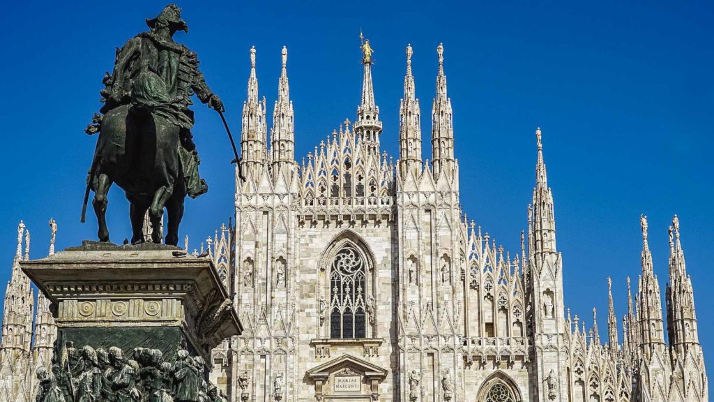 Una visione parziale sulla bellissima facciata del Duomo di Milano con le sue altissime guglie. Sulla destra spicca in primo piano la statua di Vittorio Emanuele che indica con la spada il Duomo.
