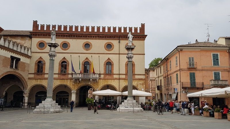 La grandissima e spaziosissima piazza del popolo a Ravenna con le sue due colonne principali sormontate da statue in marmo. Dietro il palazzo comunale con il tetto a guglie. Una piazza da vedere a Ravenna in un giorno!