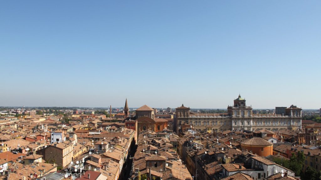 Una meravigliosa vista dall'alto di Modena su cui spicca in primo piano la sfarzosa facciata del palazzo ducale estense e il campanile di una chiesa.