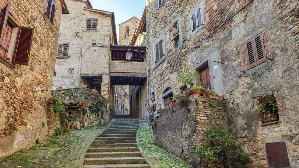 Una via scalinata circondata da case in pietra, che porta alla torre dell'orologio di Anghiari il paese della battaglia. In fondo c'è un passaggio sopraelevato coperto che collega due abitazioni.
