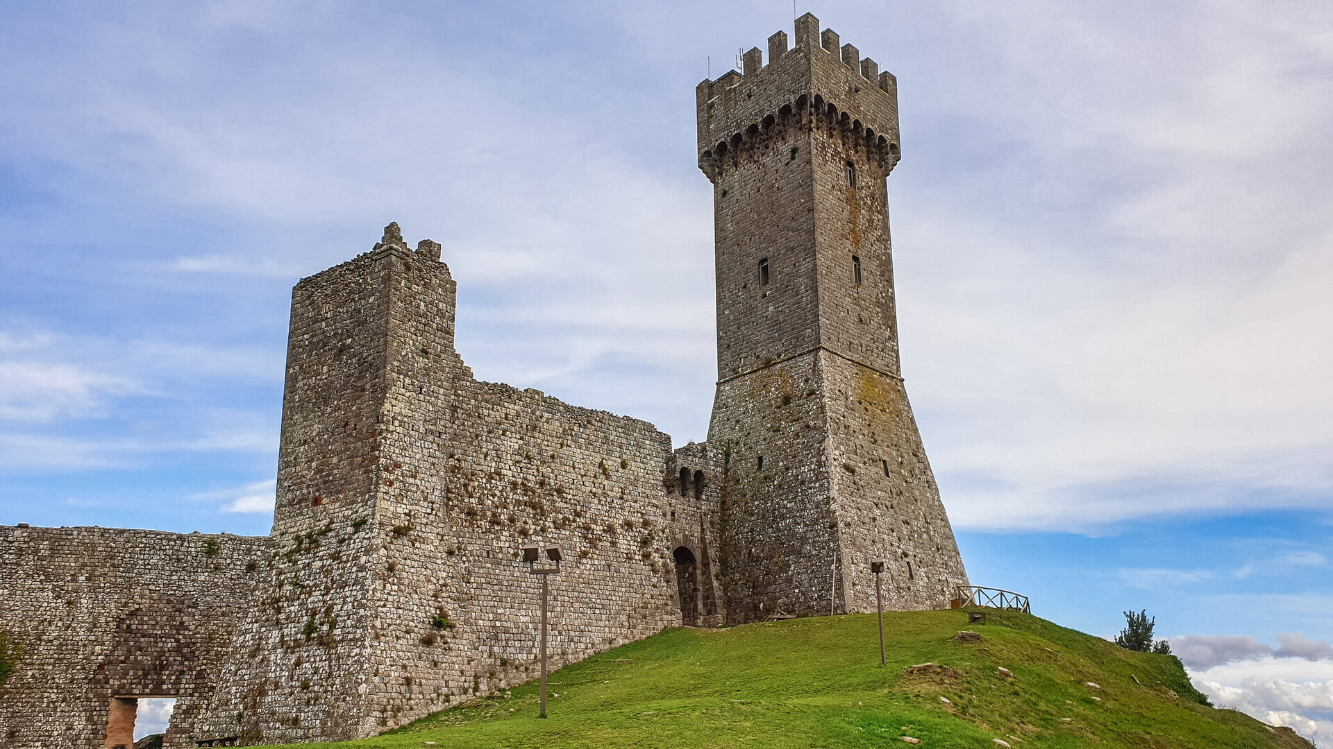 L'alto mastio dell'antico castello di Radicofani che si staglia su un cielo azzurro sereno e si appoggia su un colle verde. Accanto i resti ancora in piedi delle mura difensive.