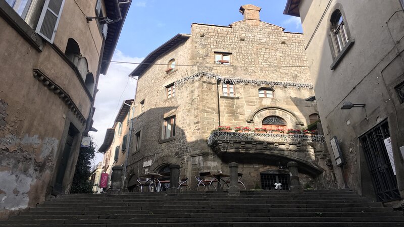 un bellissimo vicolo di Viterbo dove si può notare una rampa di scale in primo piano che porta verso edifici costruiti con in pietra grigia.