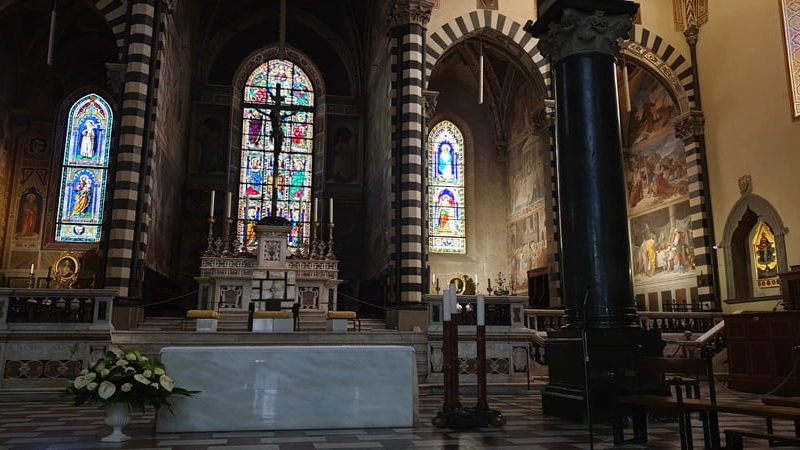 l'altare del duomo di prato con sullo sfondo le grandissime vetrate colorate, in primo piano il cristo in legno e sulla sinistra e destra le cappelle affrescate.