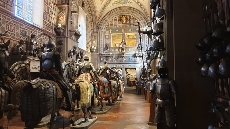uno scorcio della sala della cavalcata del museo stibbert. Si vedono dodici cavalieri con le loro armature disposti in due file orizzontali. Sulla sinistra appese al muro altre armature e spade.