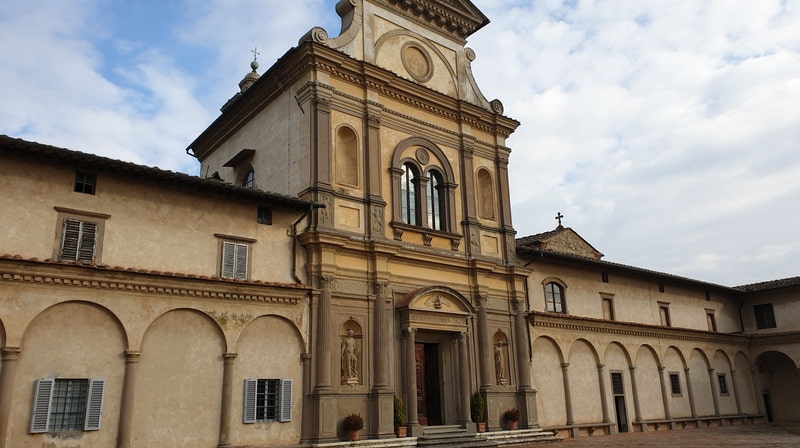 la grande e bellissima facciata della chiesa monumentale della certosa di firenze con le sue nicchie e la grande porta d'ingresso in legno