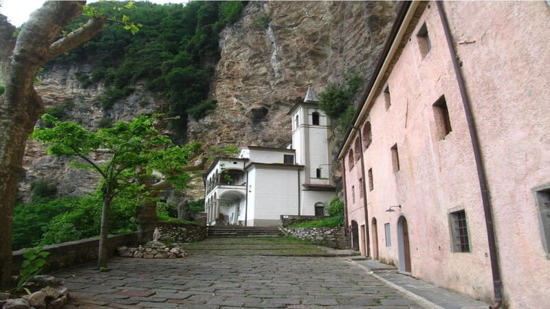 la strada che porta dall'ingresso alla chiesa dell'eremo di calomini con sulla destra il verde rigoglioso e sulla sinistra l'ingresso alla grotta. In cima si nota la roccia della montagna