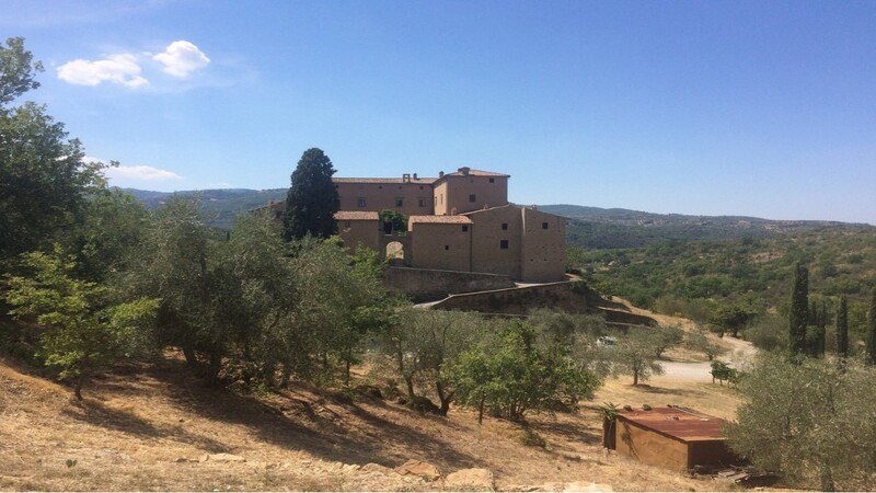 il castello del potentino visto da lontano immerso nella natura con tanti olivi intorno e campi coltivati. La struttura è costruita in pietra e presenta una grande entrata