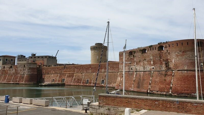la fortezza vecchia di livorno con in primo piano le sue imponenti mura poste davanti l'acqua del mare e alcune barche e sullo sfondo l'alta torre difensiva