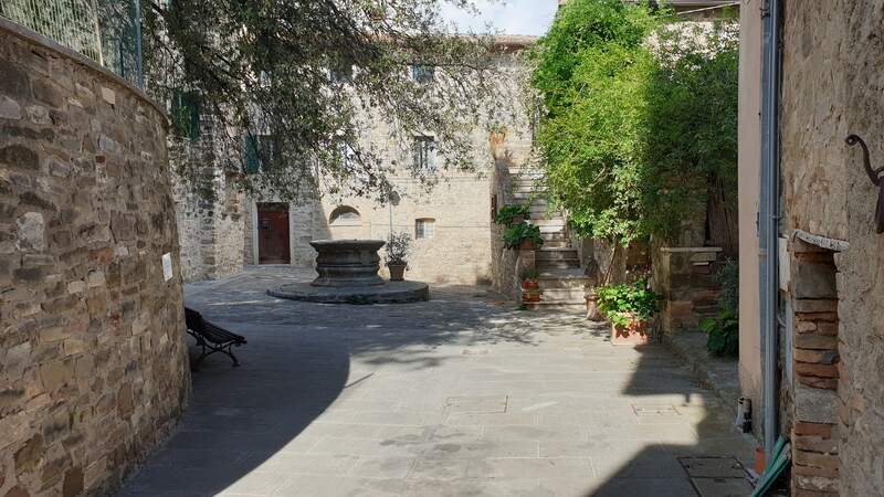 una strada contornata da muriccioli in pietra e case che porta verso una piazza con al centro un pozzo medievale