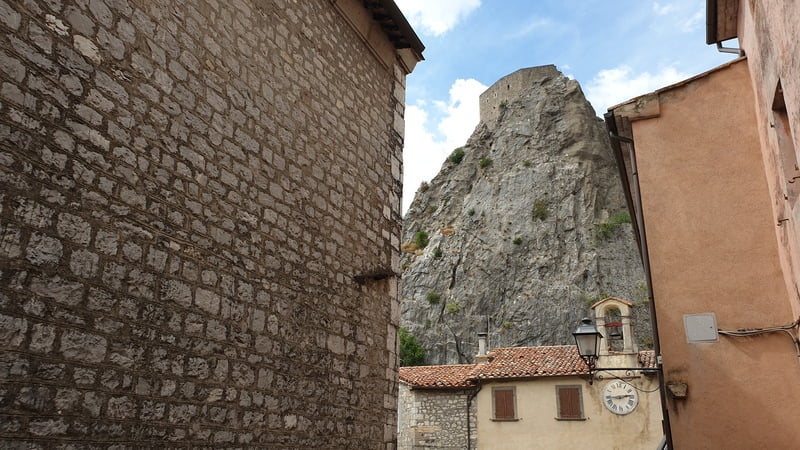 la rocca di roccalbegna vista da una viuzza del centro storico che spicca sopra lo sperone roccioso della montagna con le sue imponenti mura e le feritoie