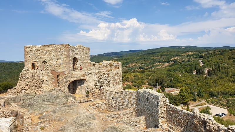 la tore quadrangolare della rocca di montemassi contornata dai resti delle antiche mura medievali e con dietro il verde della collina della maremma