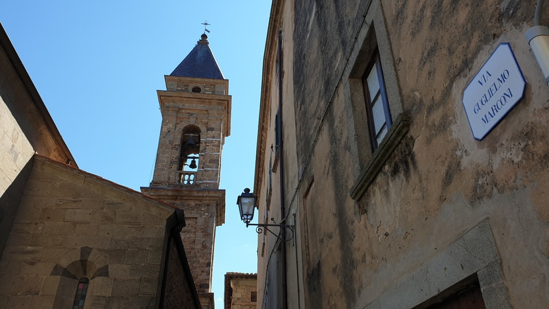 una vista da lontano da una delle strade del centro storico di seggiano sul retro della chiesa di san bartolomeo e sull'alto campanile con la torre a punta