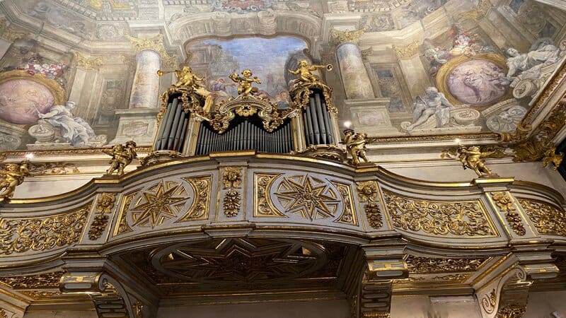 un primo piano sull'organo della cappella dei mercanti di torino con le sue decorazioni in oro e i tanti puttini rappresentati. Sullo sfondo parte degli affreschi che decorano la volta
