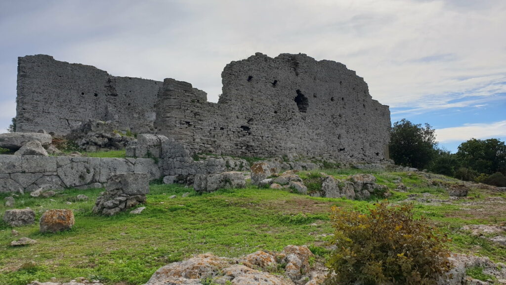 una vista in lontananza sui maestosi resti del tempio di giove con sullo sfondo il blu dell'acqua della laguna di orbetello e davanti il verde rigoglioso della natura