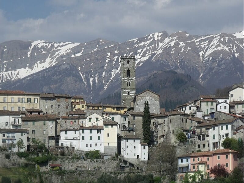 una vista da lontano su uno dei borghi toscani da vederem coreglia anteminelli con sullo sfondo le alpi apuane completamente innevate. Al centro dell'immagine spicca la chiesa della città con l'alta torre campanaria medievale