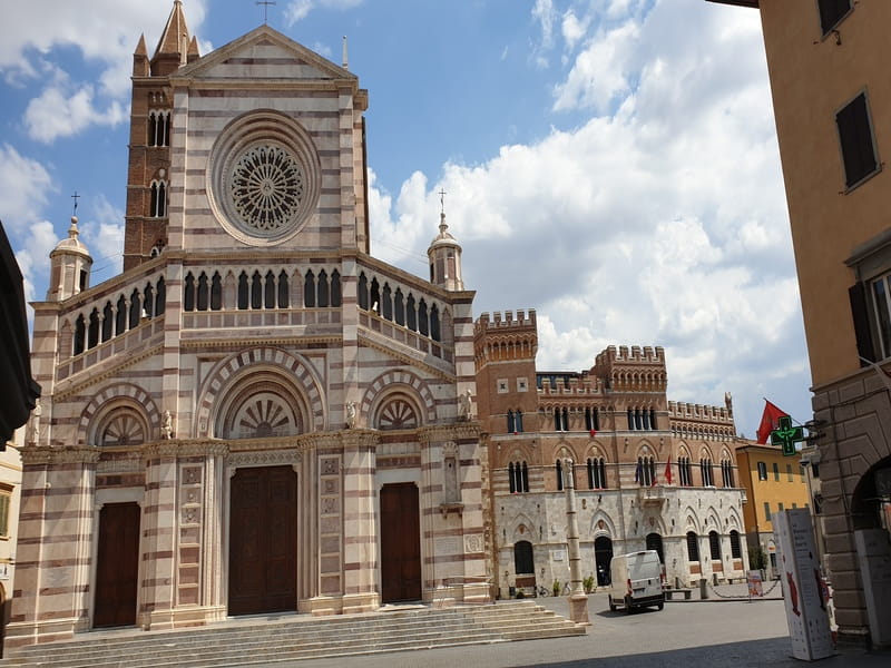 Facciata del Duomo di Grosseto con rosone e torre campanaria, accanto agli edifici di Piazza Dante