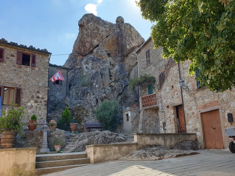 Piazza centrale di Roccatederighi con abitazioni in pietra e rupe naturale sullo sfondo, un perfetto esempio di cosa vedere in Maremma più autentica